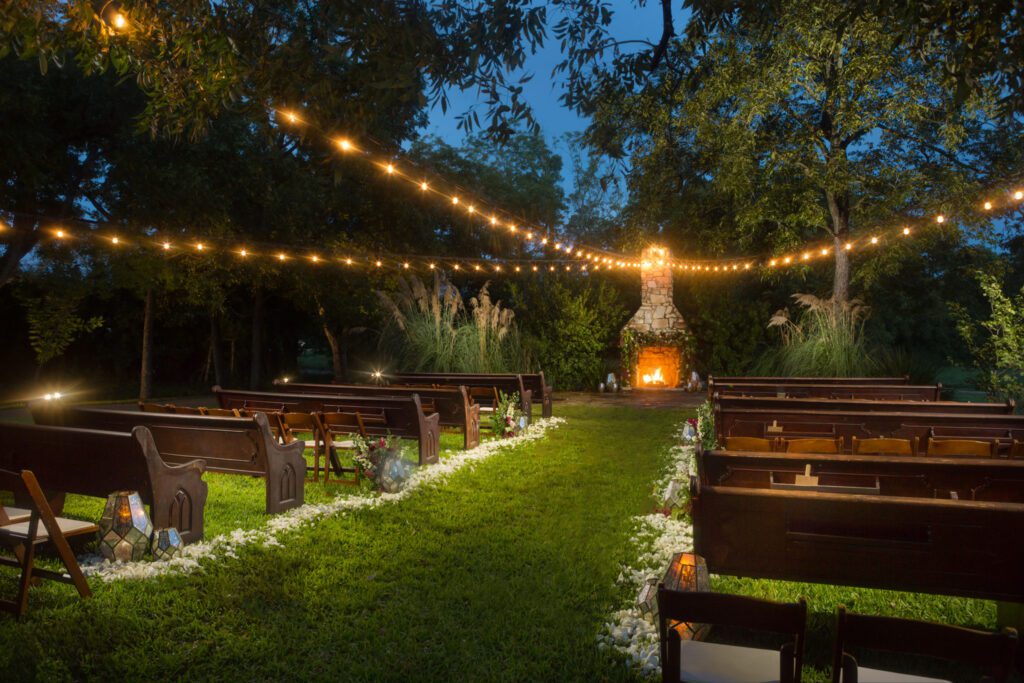 Outdoor ceremony with string lights and fireplace backdrop at dusk