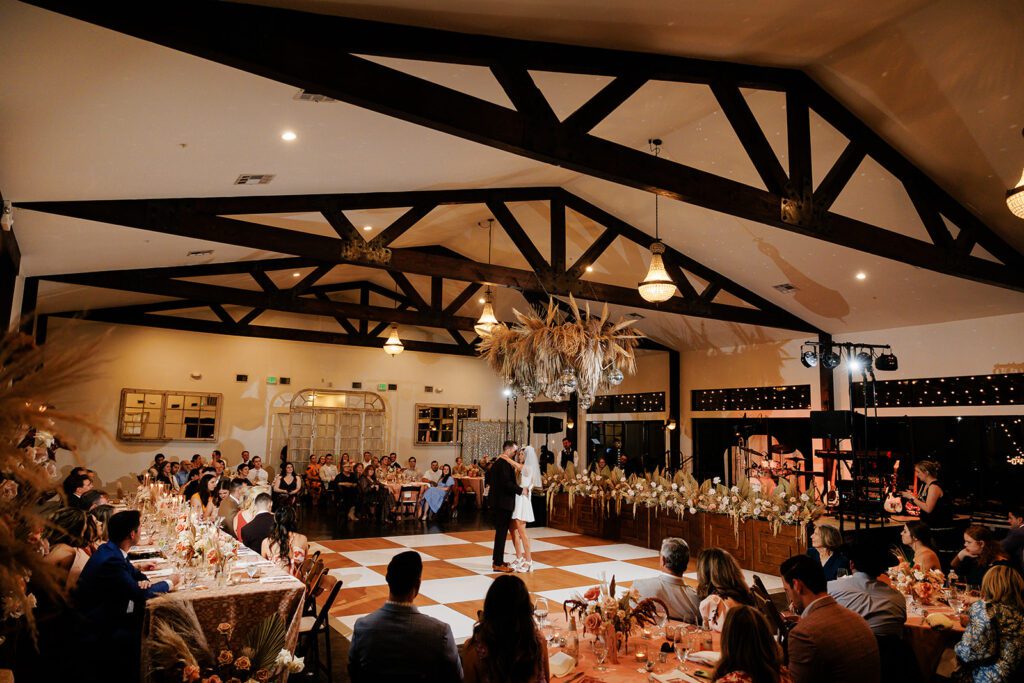 Indoor reception with guests and dance floor under wooden beams