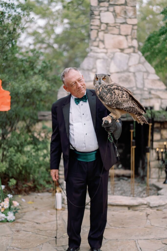 Man in tuxedo holding owl near stone fireplace