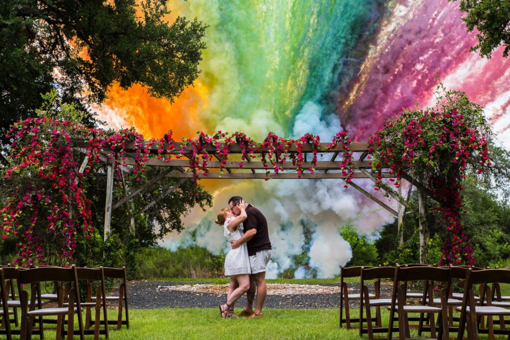 Couple kissing under floral arbor with colorful smoke backdrop