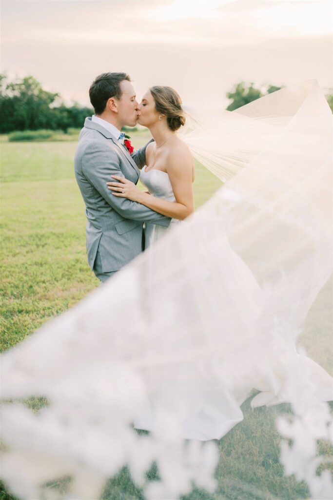 Couple kissing with veil flowing in outdoor field