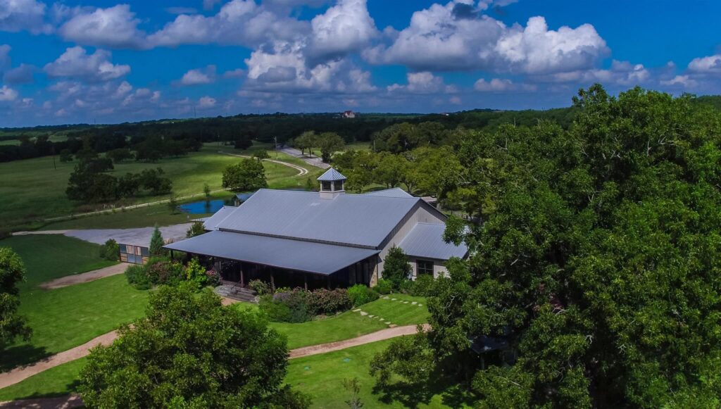 Aerial view of an austin wedding venue surrounded by trees and open fields under a blue sky