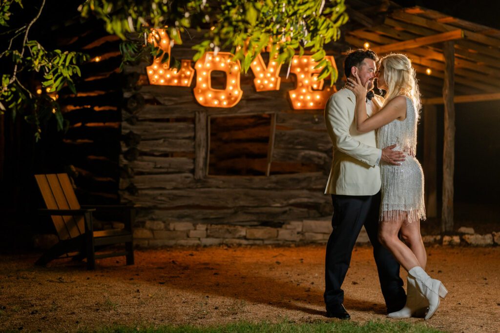 Couple kissing under illuminated LOVE sign at night wedding