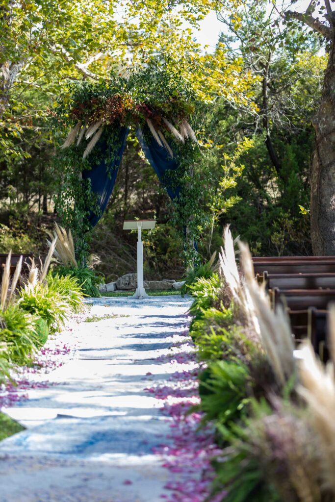 Outdoor ceremony aisle with greenery arch and blue draping