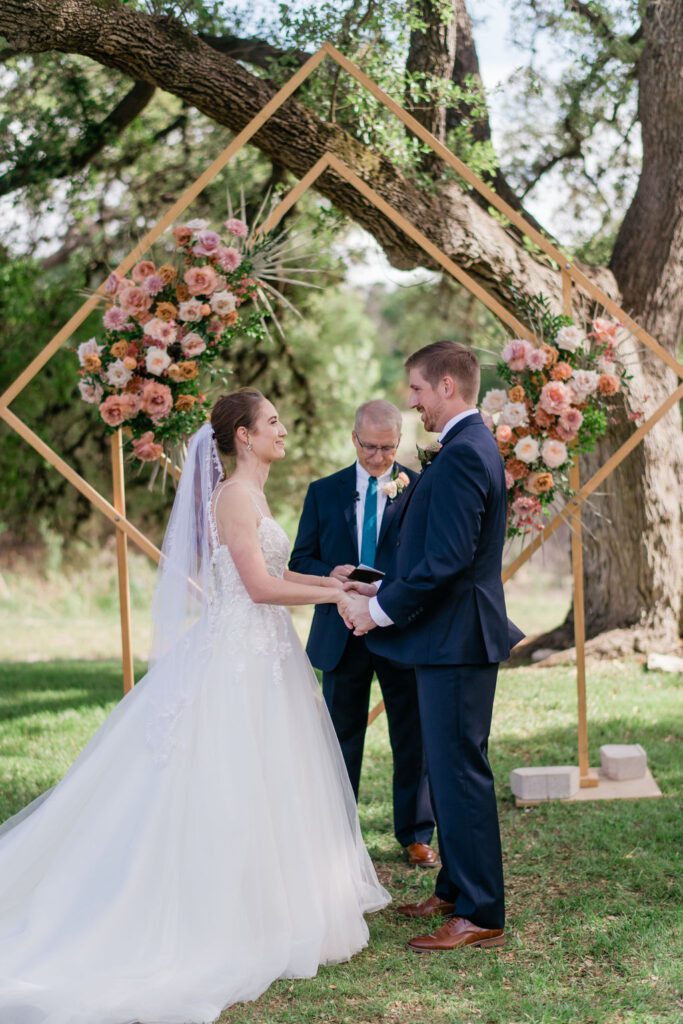 Bride and groom exchanging vows under geometric floral arch