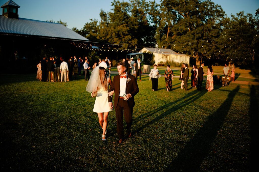 Bride and groom happily walking holding drinks with he guests in the background during cocktail hour