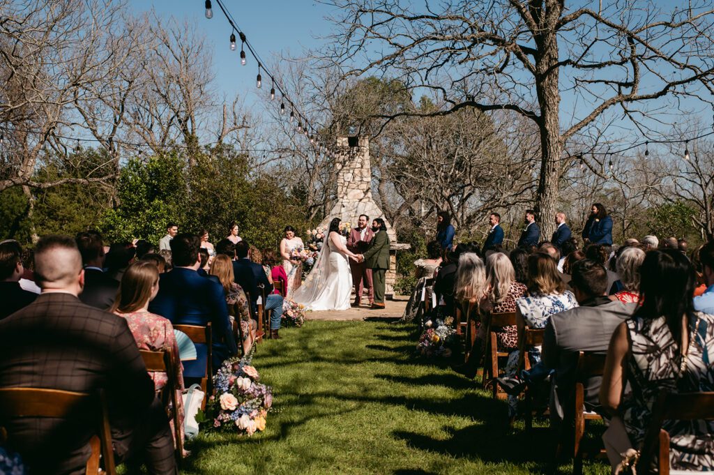 Outdoor wedding ceremony with string lights and stone fireplace backdrop