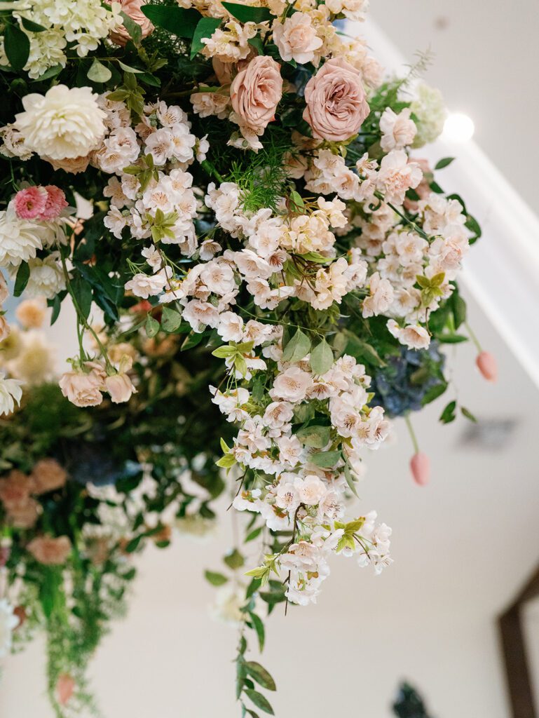 Close-up of a hanging floral arrangement with blush garden roses, white blossom branches, cream dahlias and trailing greenery