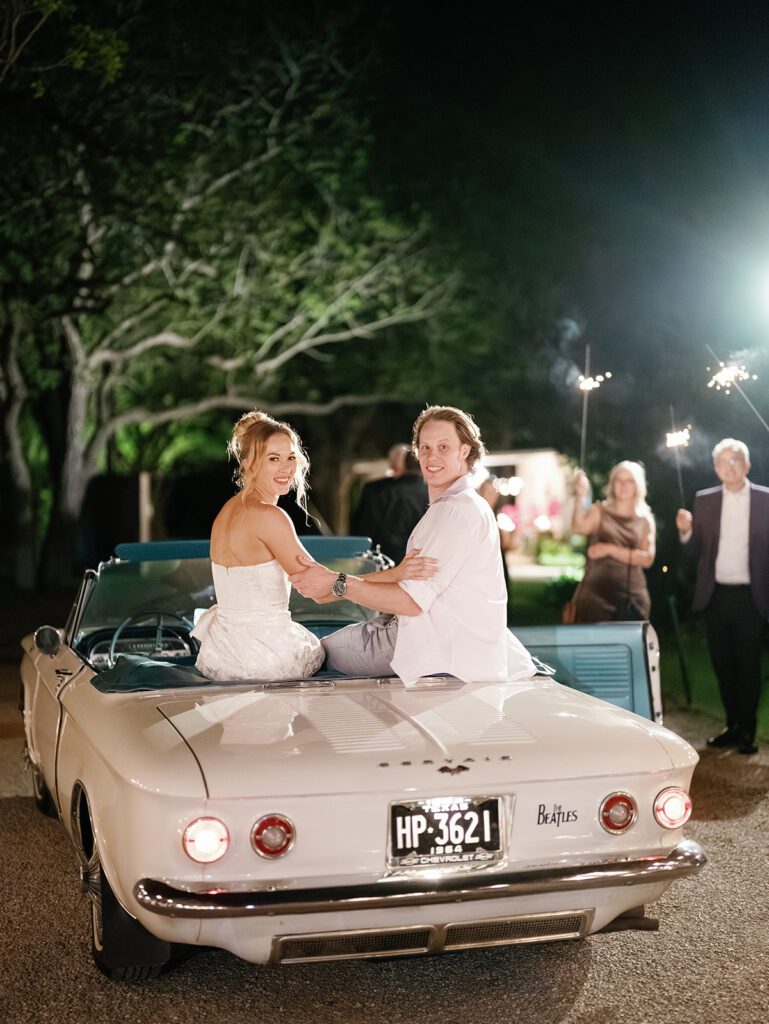 Newlyweds sitting on vintage convertible after sparkler exit